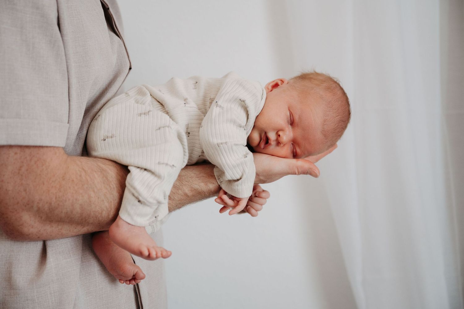 A series of hands gently holding and supporting a sleeping newborn baby against a light background.