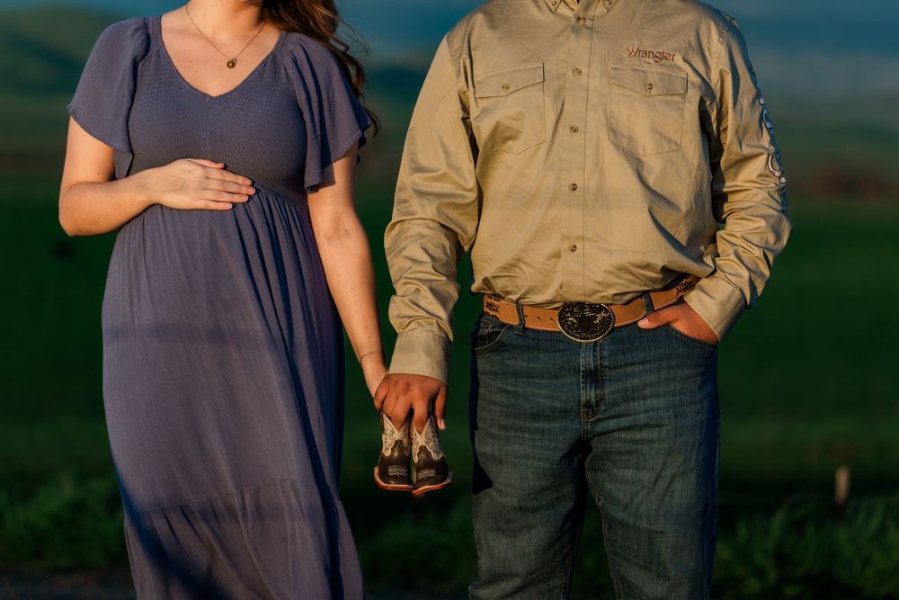 A couple stands together in a rustic outdoor setting during golden hour with mountains in the background.