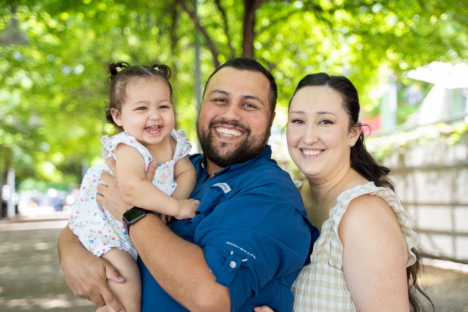 Family enjoying a candid outdoor photoshoot in a park setting with lush green trees in the background.