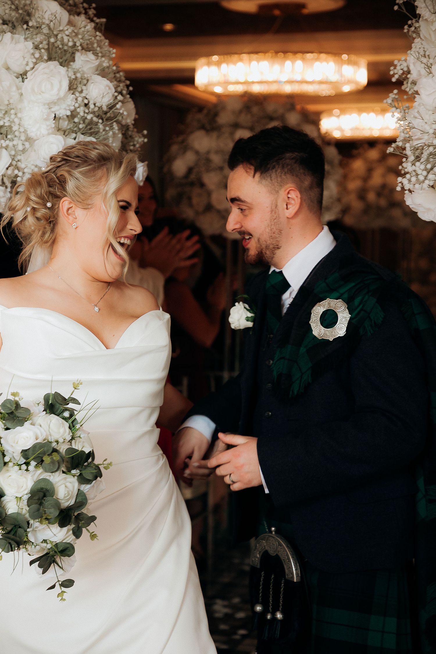 Candid wedding moment under floral arch with Scottish tartan details.