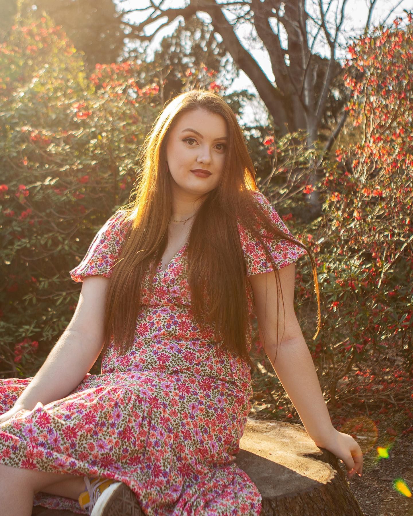 Portrait of a young woman in a floral dress sitting among spring blossoms at sunset.