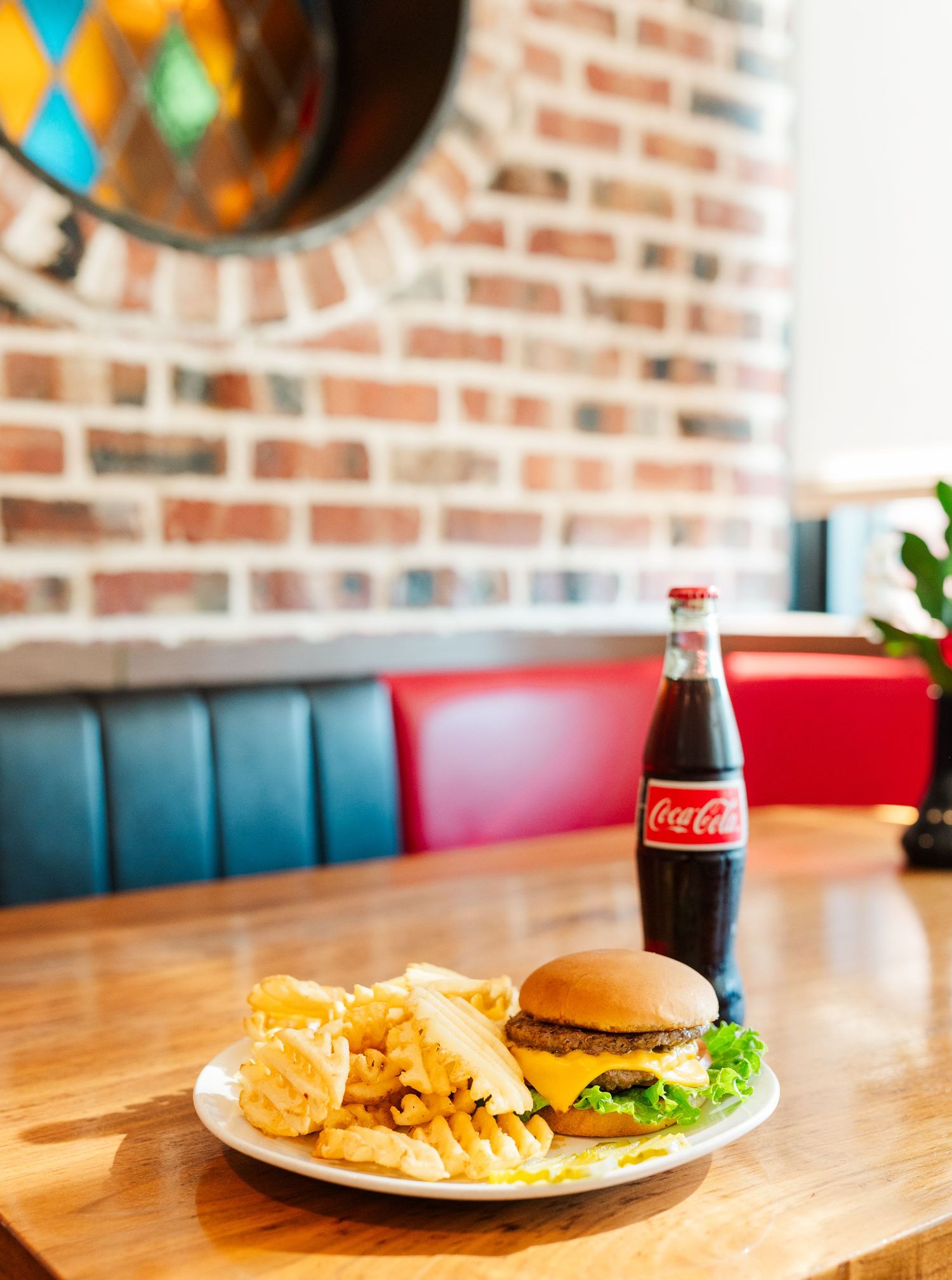 Cheeseburger and potato chips served on white plate with Coca-Cola bottle.