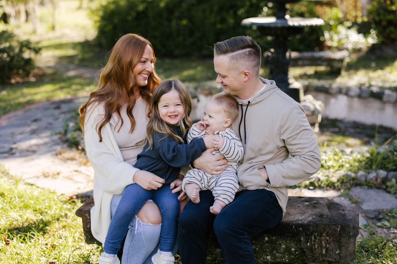 Family shares tender moments together while sitting outdoors in dappled sunlight on stone steps.