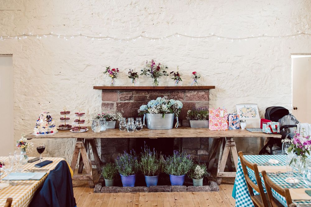 Rustic wedding decor display with wooden tables, floral arrangements, and vintage accents against a white brick wall.