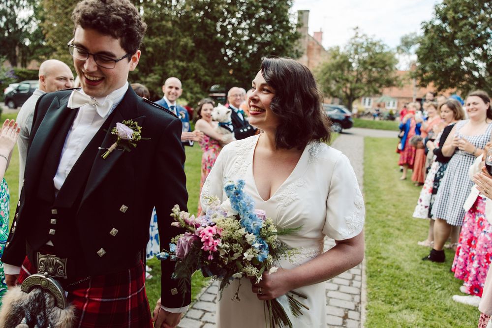 Outdoor wedding celebration with guests gathering on grassy lawn during daytime festivities.