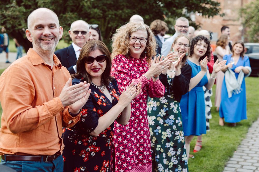 Wedding guests stand in a line outdoors clapping and celebrating during a joyful reception ceremony.