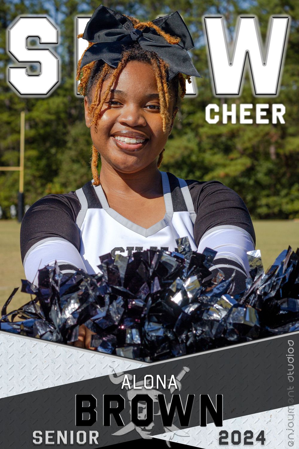 High school cheerleader in uniform poses with pom poms against outdoor background for senior photos.
