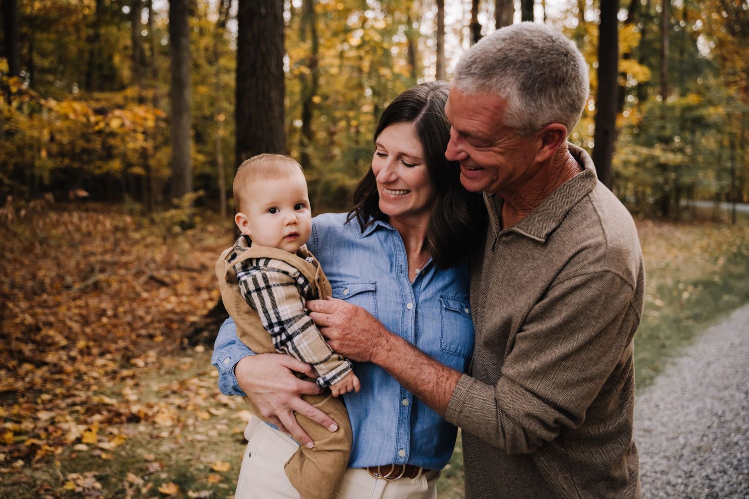 proud grandparents and baby enjoying a tender moment together on an autumn path surrounded by golden fall foliage. Family photographer in Mi