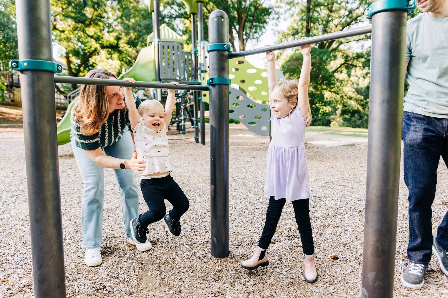 Children's feet dangle from playground equipment as they swing and play on a sunny day at an outdoor park.