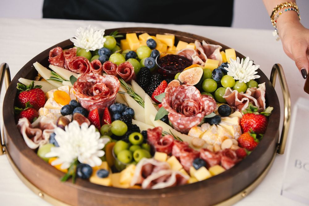 A beautifully arranged charcuterie board with meats, cheeses, fruits, and flowers displayed in a circular pattern.