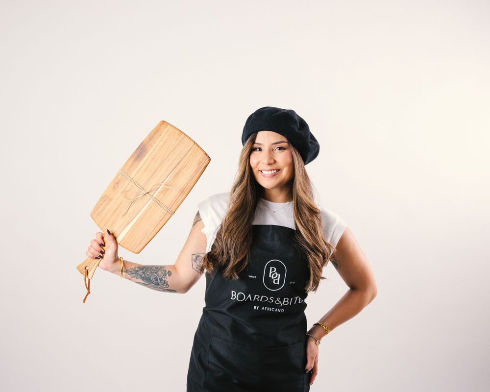 Woman in black t-shirt and beret holds wooden cutting board against white background.