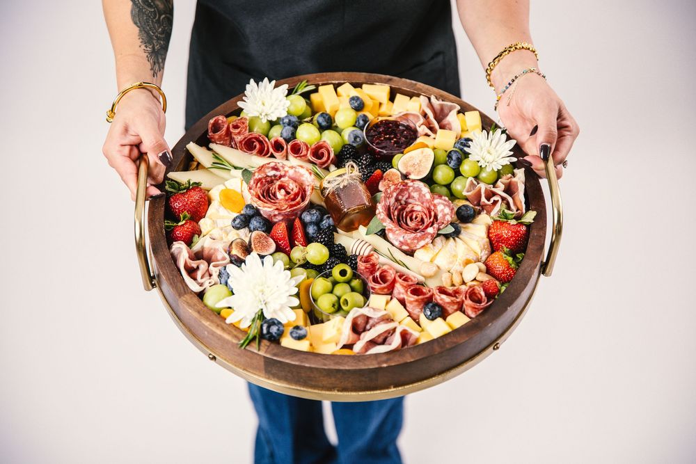 Overhead view of colorful charcuterie board with meats, cheeses, fruits and flowers arranged artistically.