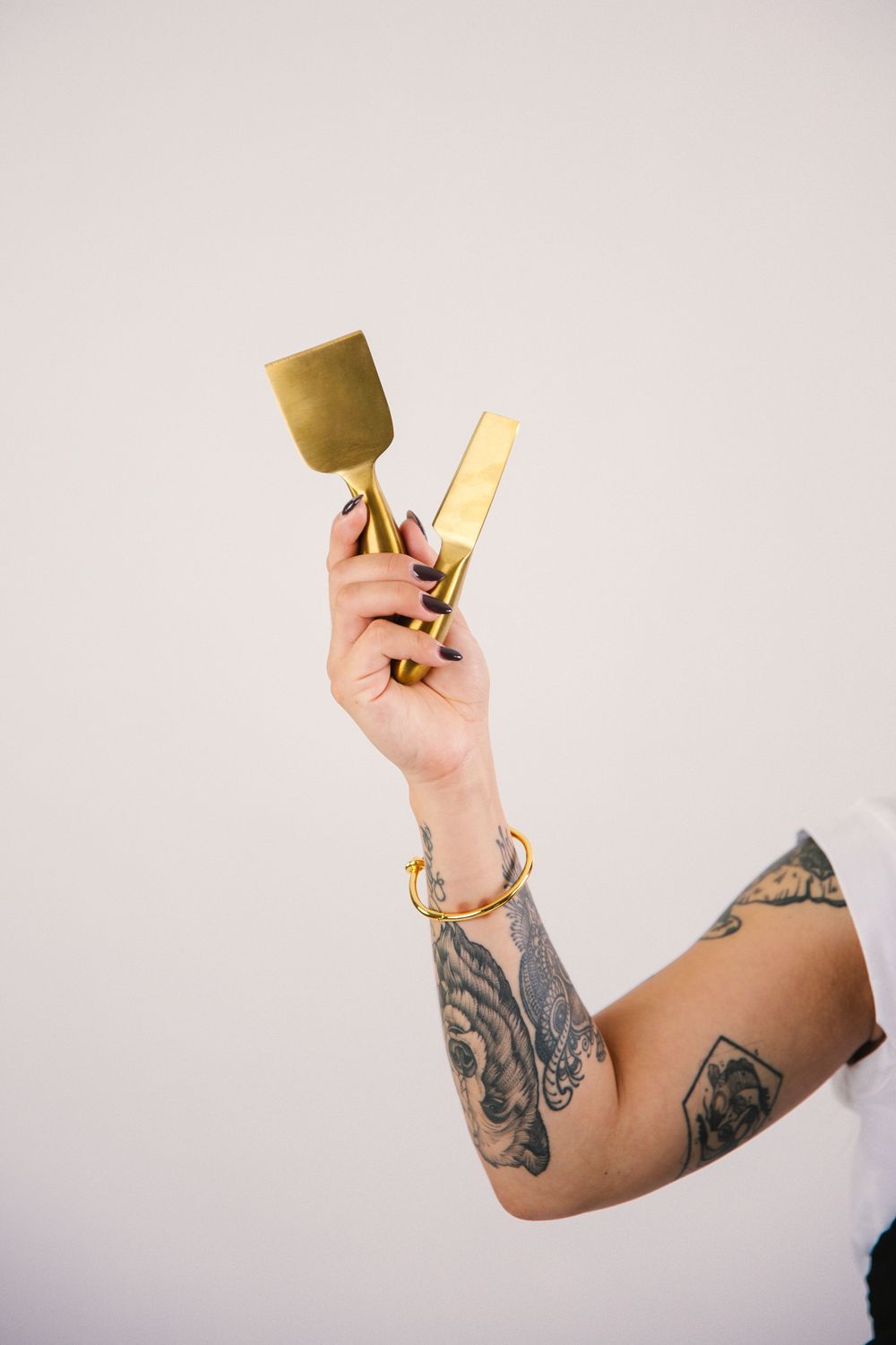Tattooed arm holding up a golden trophy cup against a white background.