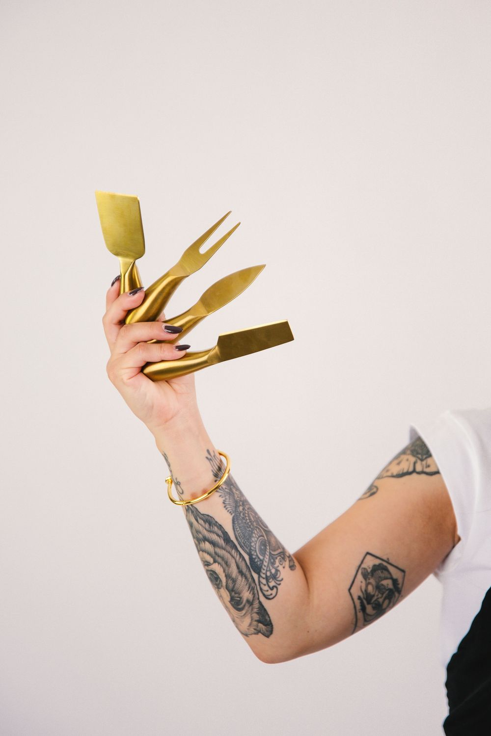 Tattooed arms holding golden serving utensils against a white background.