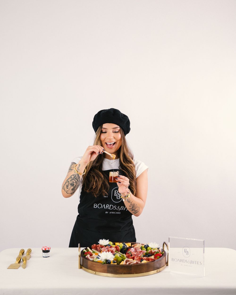 Person in black beret and tank top posing with dessert platter on white background.
