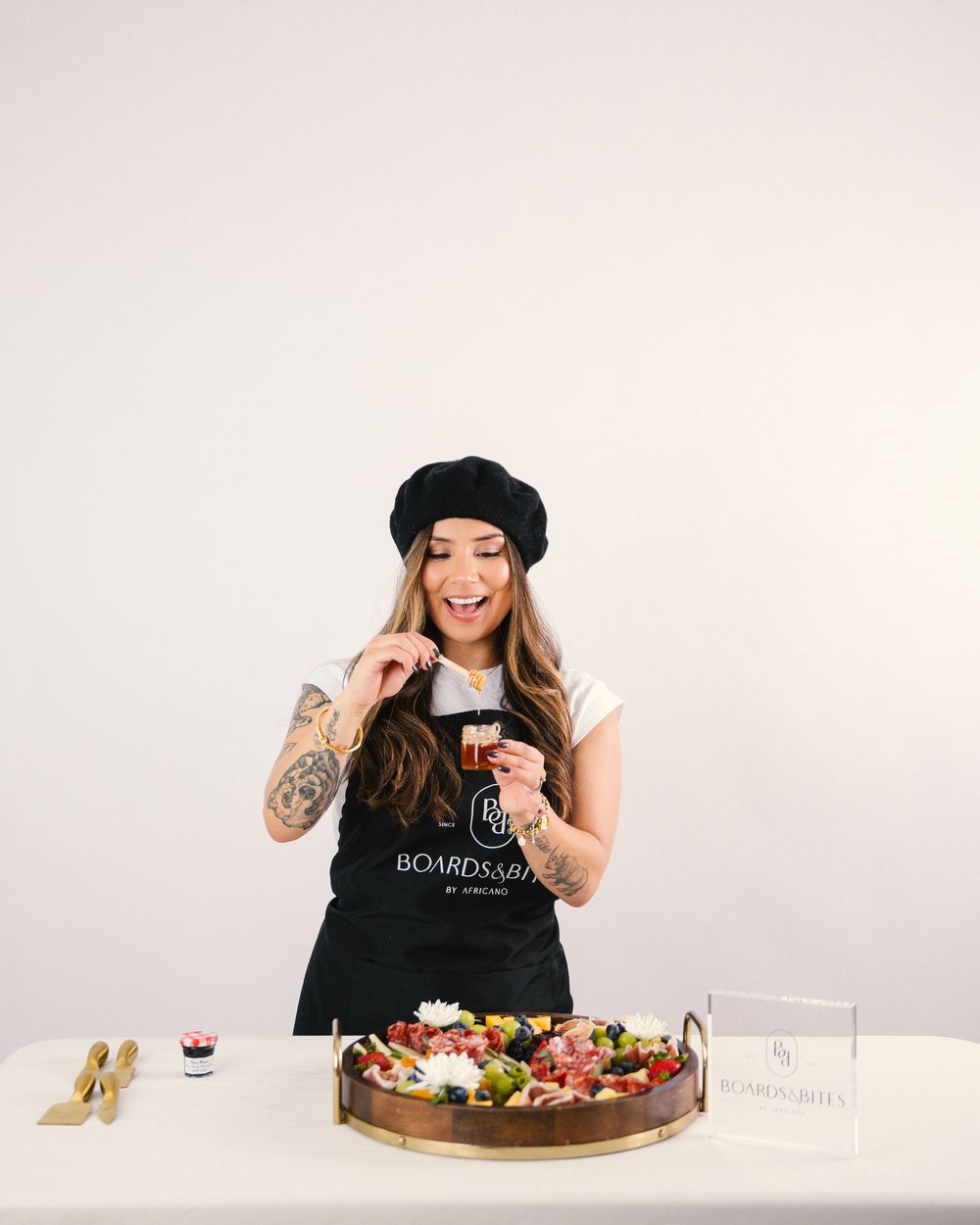 Person in black beret and tank top gesturing excitedly near a decorated dessert platter.