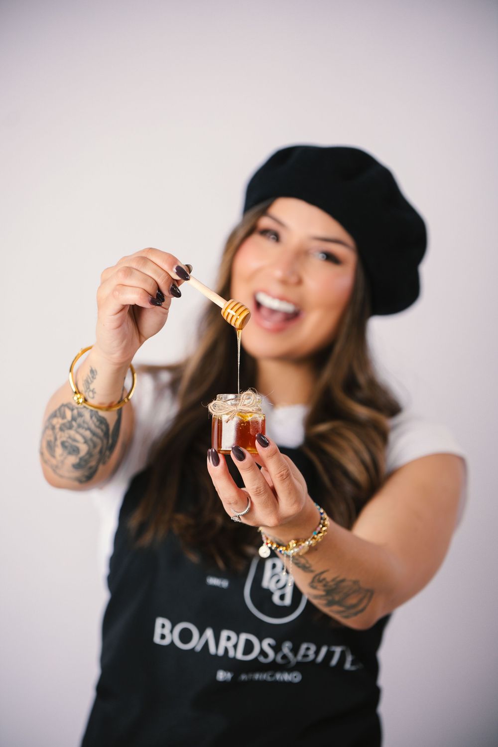 Woman in black t-shirt and beanie holding up small glass bottles against white background.