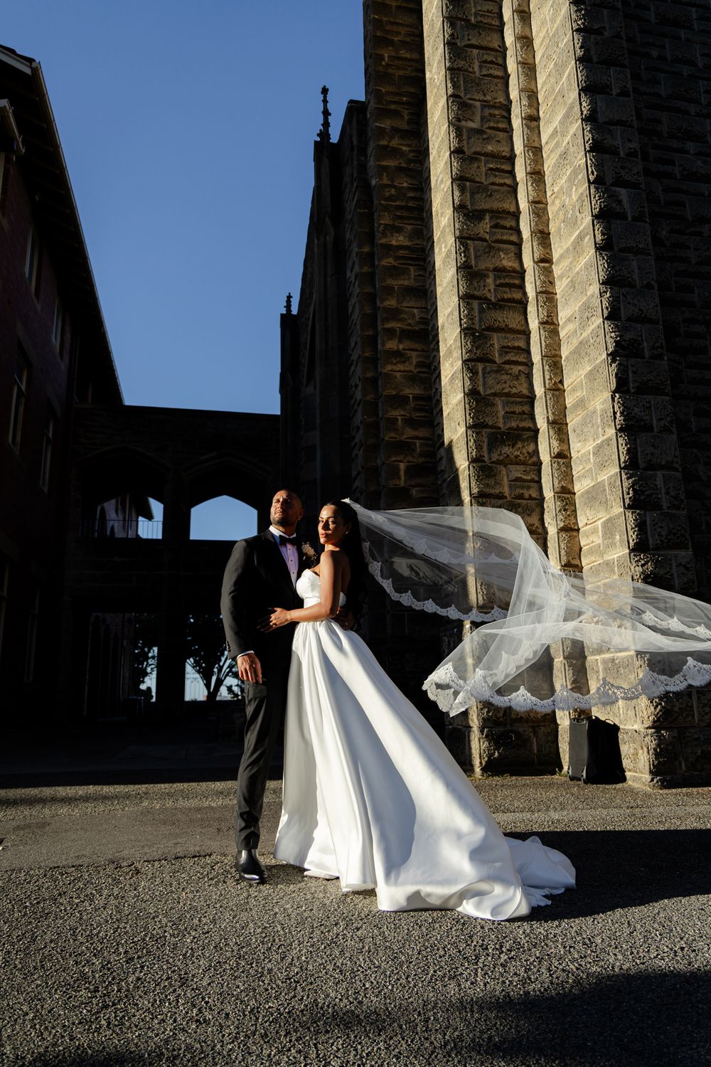 A bride in a flowing white wedding dress poses dramatically against stone columns at a historic venue.