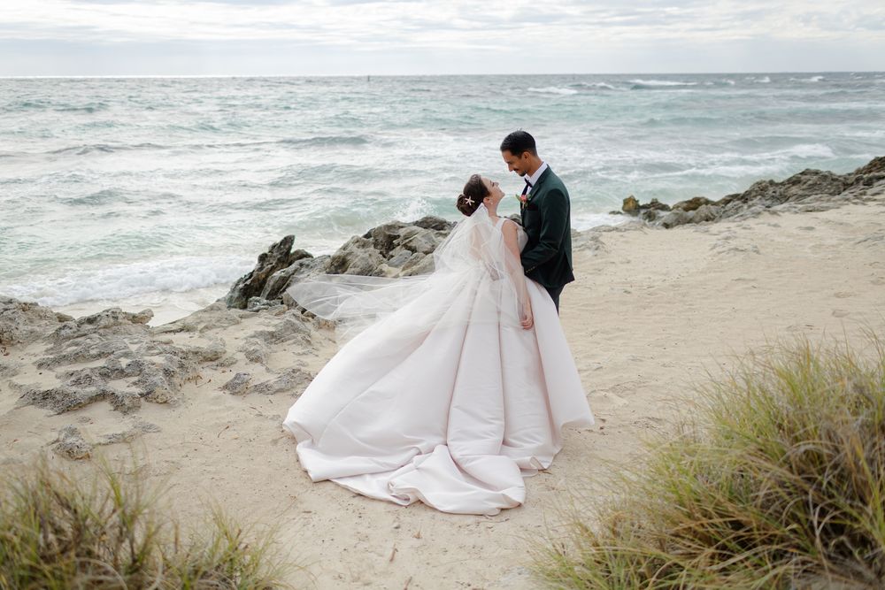 Romantic coastal wedding photoshoot featuring elegant couple walking along beach with dramatic ocean waves.