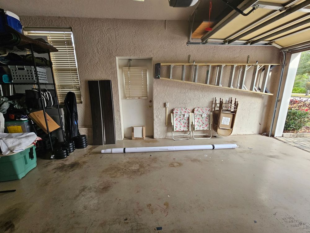 Interior view of a cluttered residential garage with storage boxes, tools, and equipment along the walls.