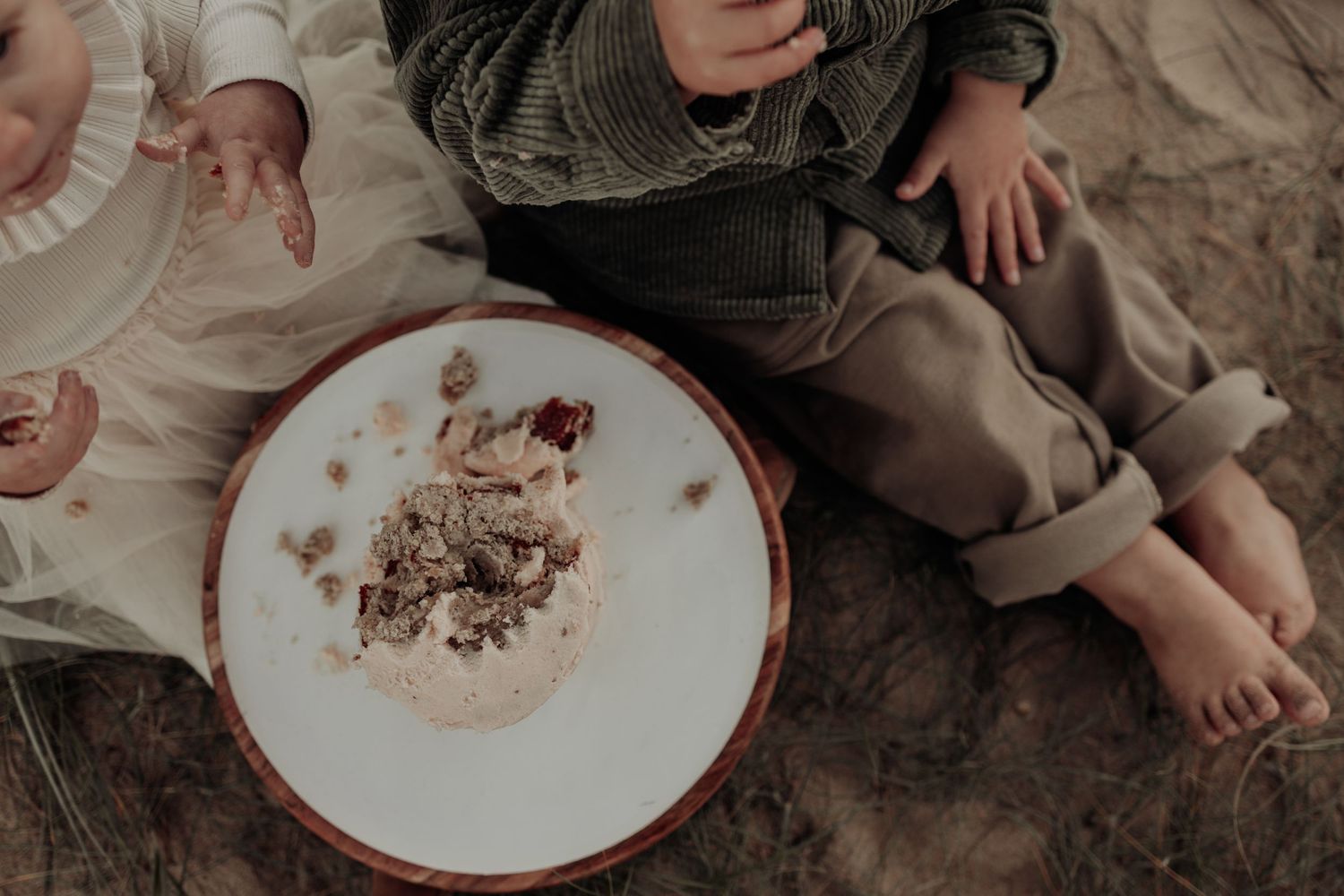 Two young children sitting on the ground sharing a plate of food, barefoot in casual clothing.