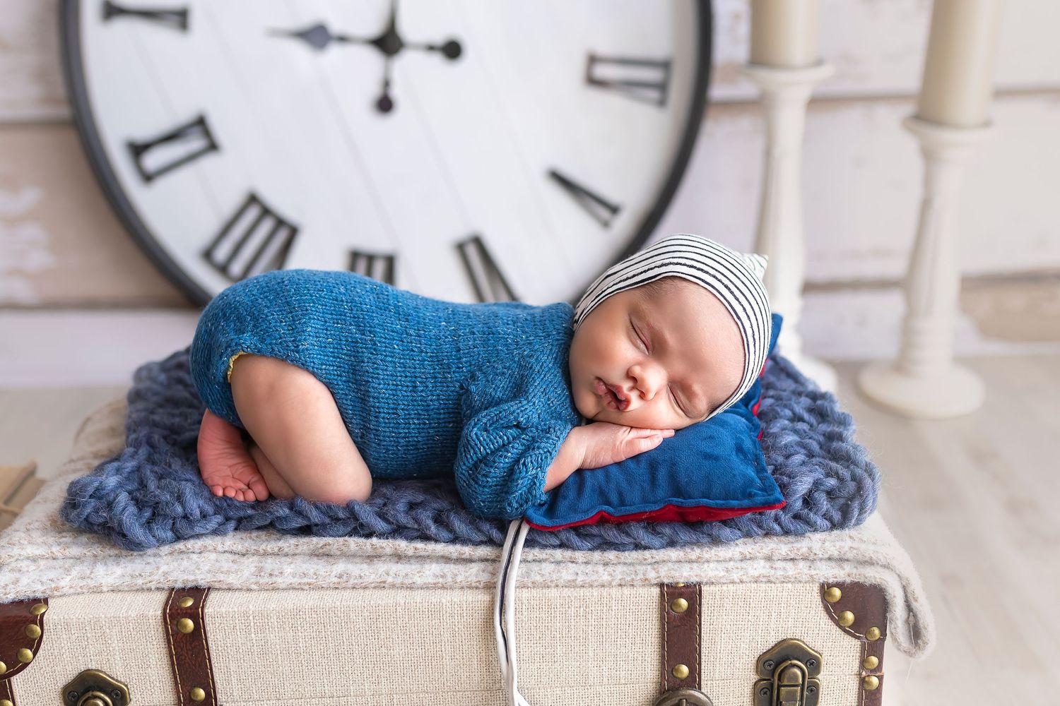 hermoso bebe duermiendo encimade una maleta antigua atras hay un reloj grande