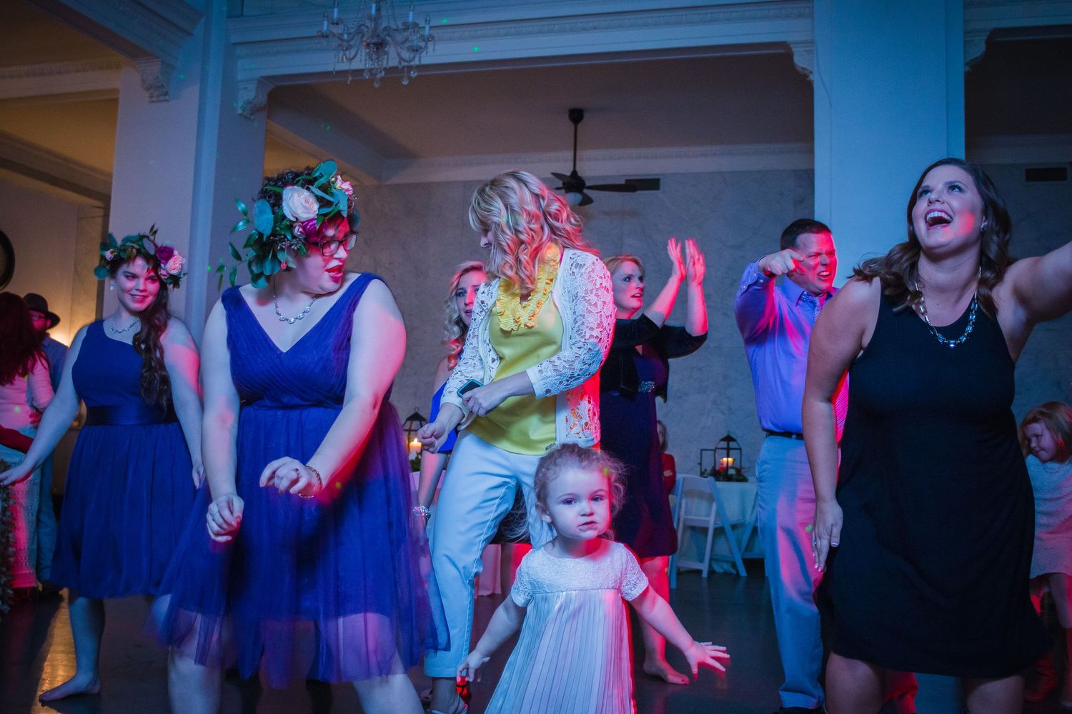 People dancing and celebrating at a wedding reception with colorful lights and festive atmosphere.