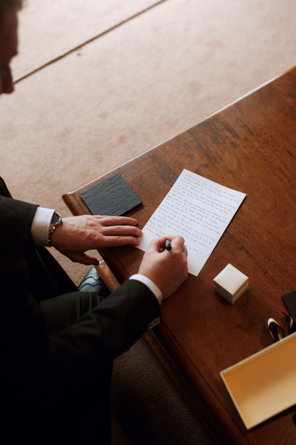 Hands writing personal wedding vows on paper at wooden desk.