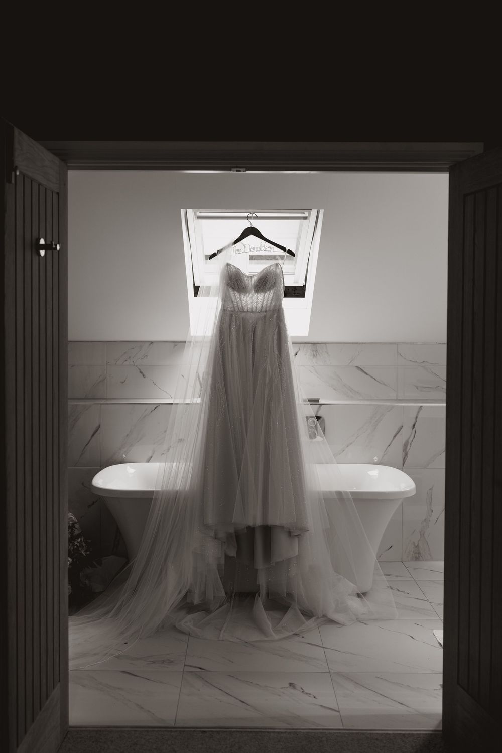 A wedding dress hanging in dramatic lighting against marble bathroom walls.