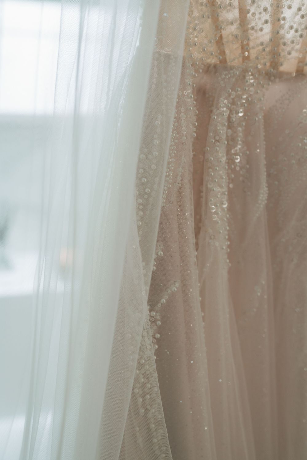 Close-up view of delicate white tulle fabric with sparkly beaded details hanging in soft window light.