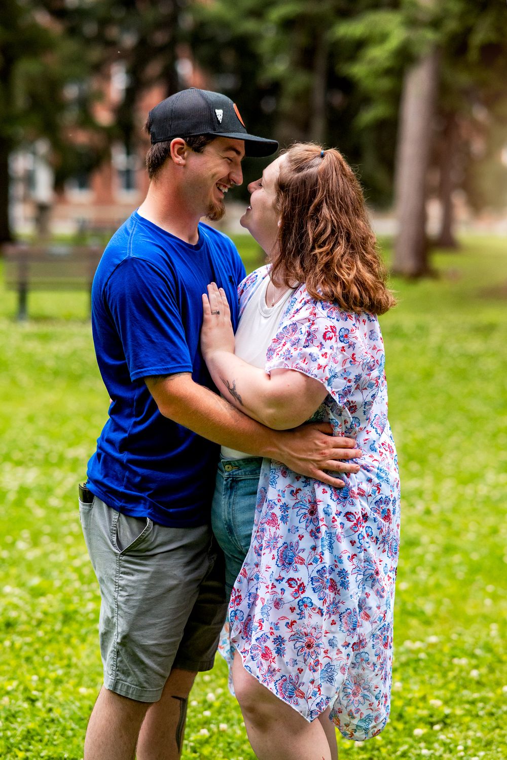 A romantic couple embraces while sharing a tender moment in a park setting with lush green grass.