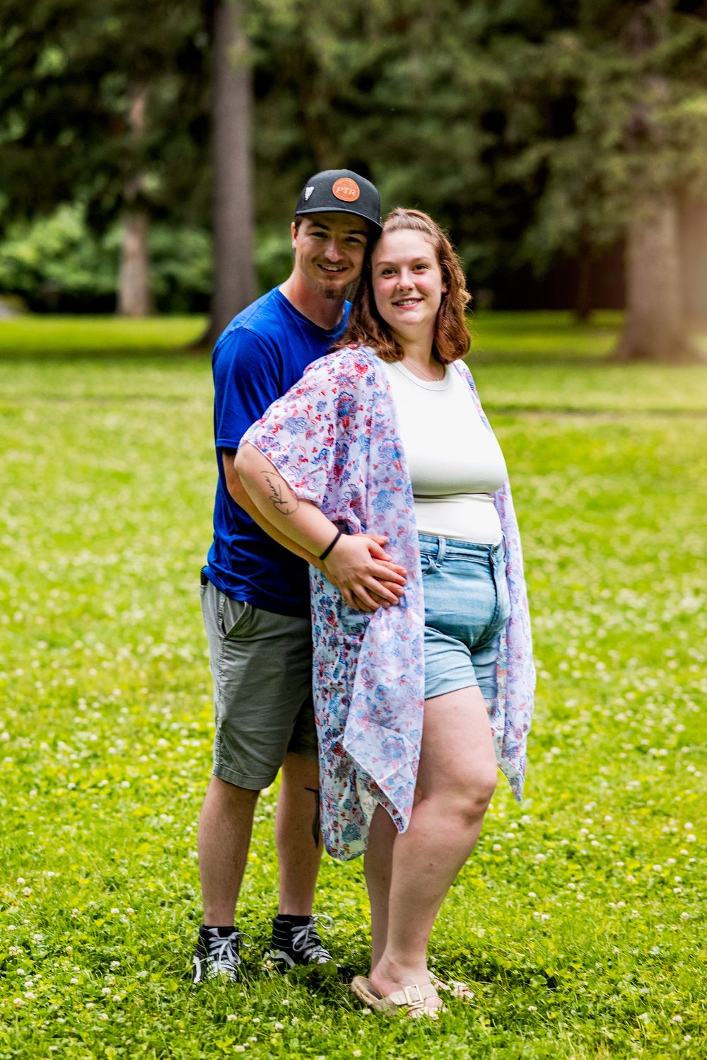 A couple poses playfully in a grassy field with white wildflowers on a sunny day.