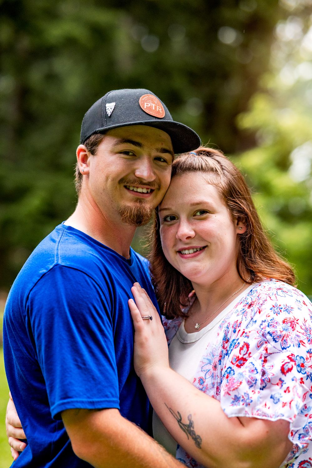 A couple in casual attire share playful moments together outdoors in a natural setting with soft lighting.