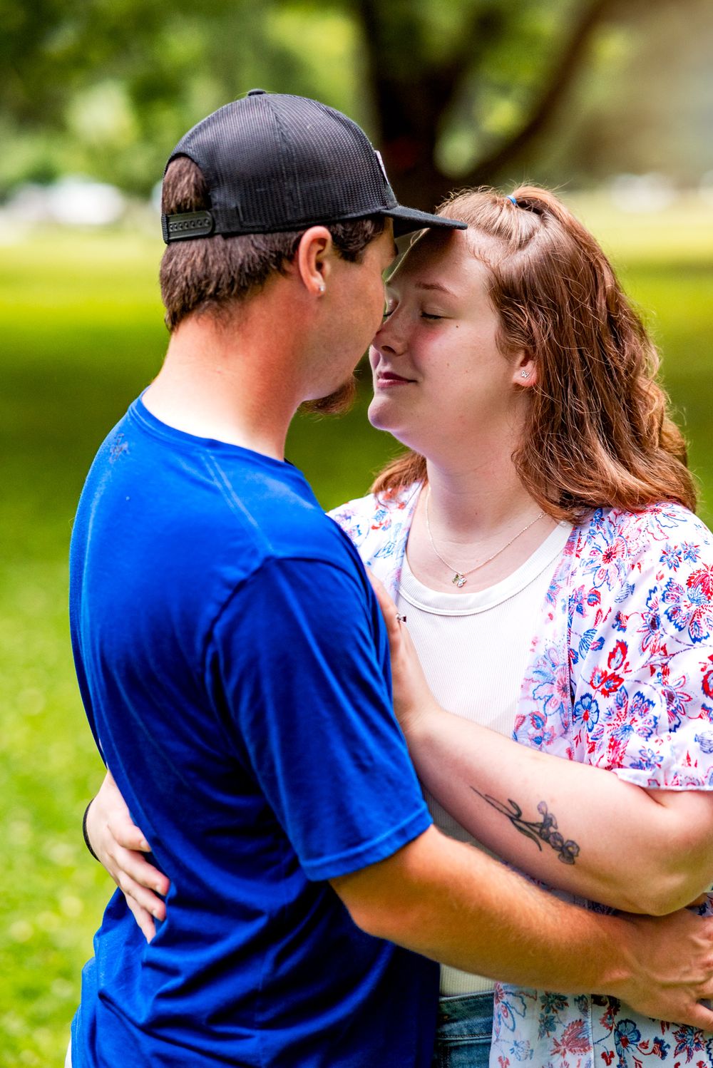 A couple in casual attire embraces lovingly in a sunny outdoor park setting.
