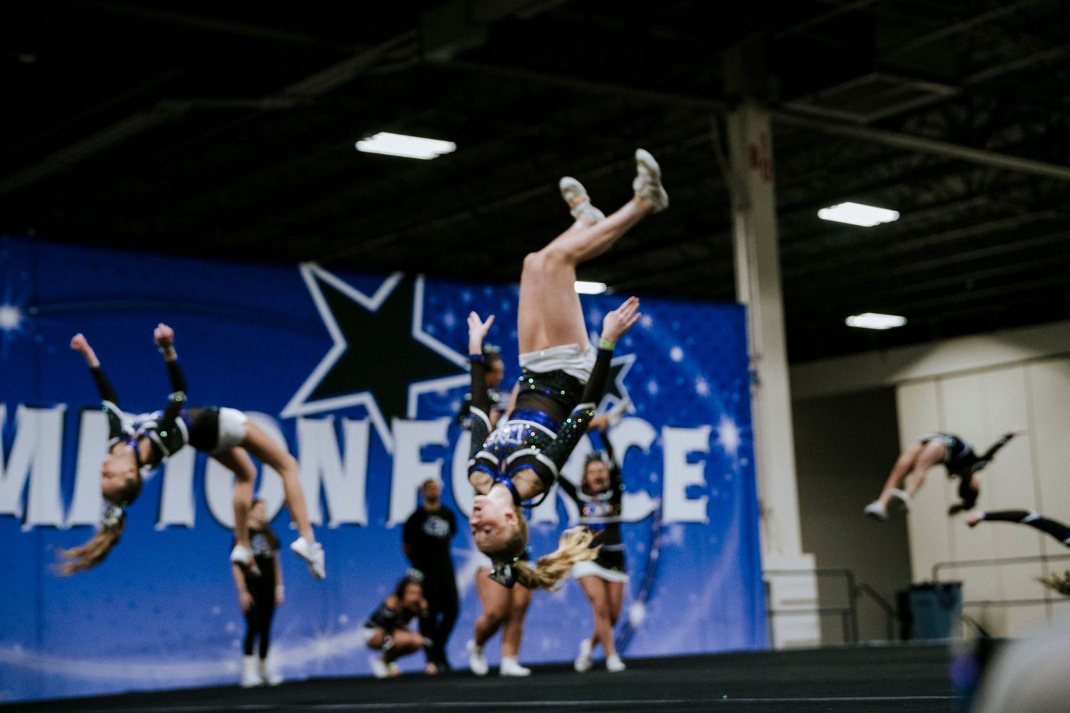 Cheerleaders perform dramatic aerial stunts during competitive routine at indoor event.