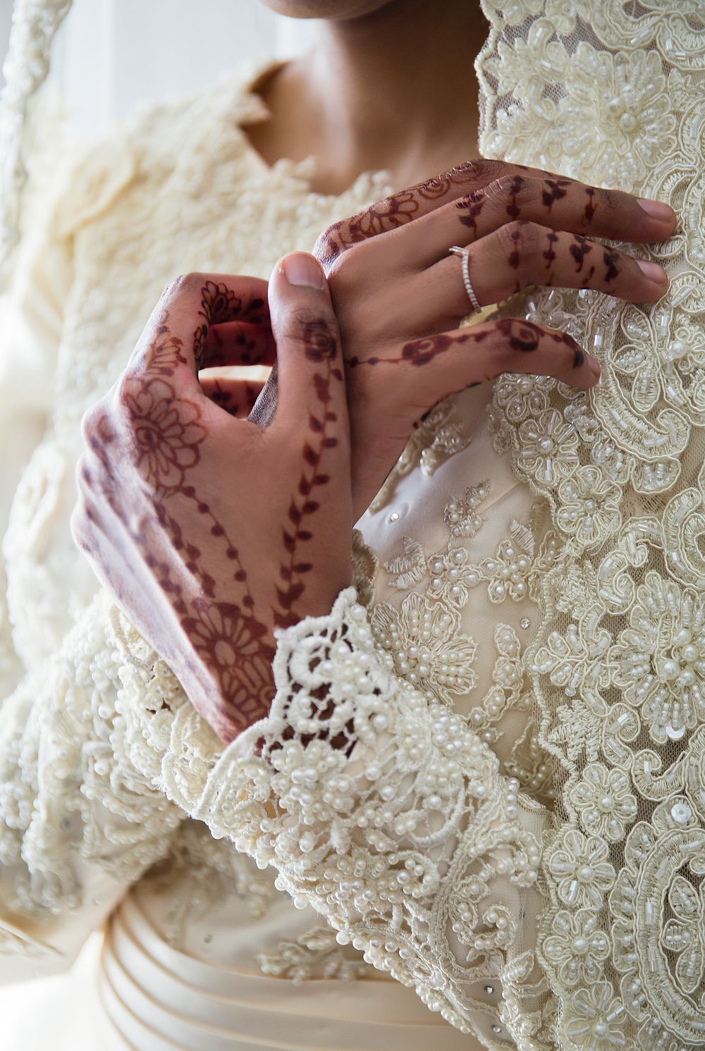 Close-up of bride's hands adorned with intricate henna mehndi designs in white lace gown.