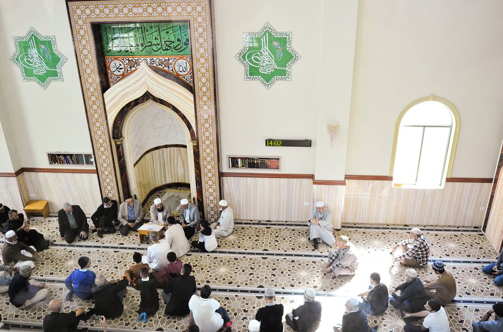 Aerial view of worshippers gathered inside a mosque with ornate Islamic architecture.
