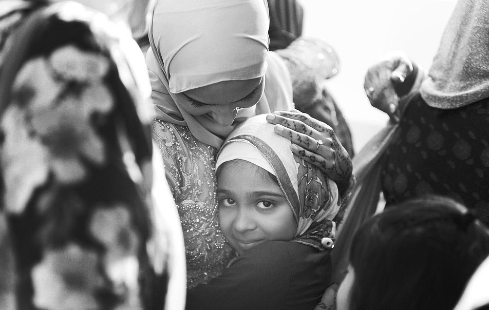 Black and white photo of two women in hijabs sharing a warm embrace at a celebration.