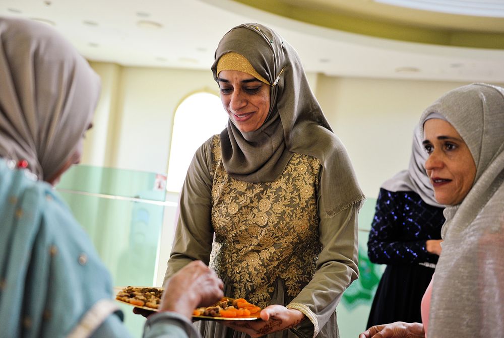 Muslim woman in hijab serving food on a platter to guests at a wedding reception.