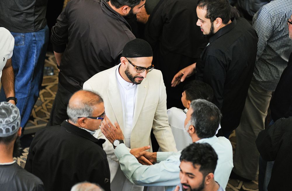 Groom in white suit greeting male wedding guests inside a mosque after Islamic wedding ceremony.