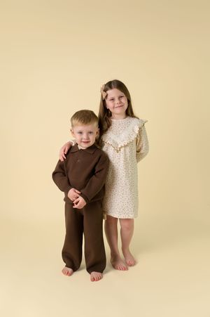 Three sequential photos showing a child in brown clothing playfully posing against a cream-colored backdrop.