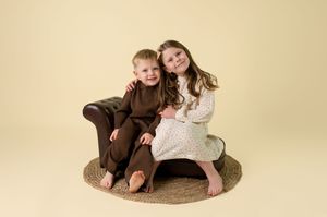 Two people in brown and white outfits pose together on a beige backdrop in a professional photo shoot.