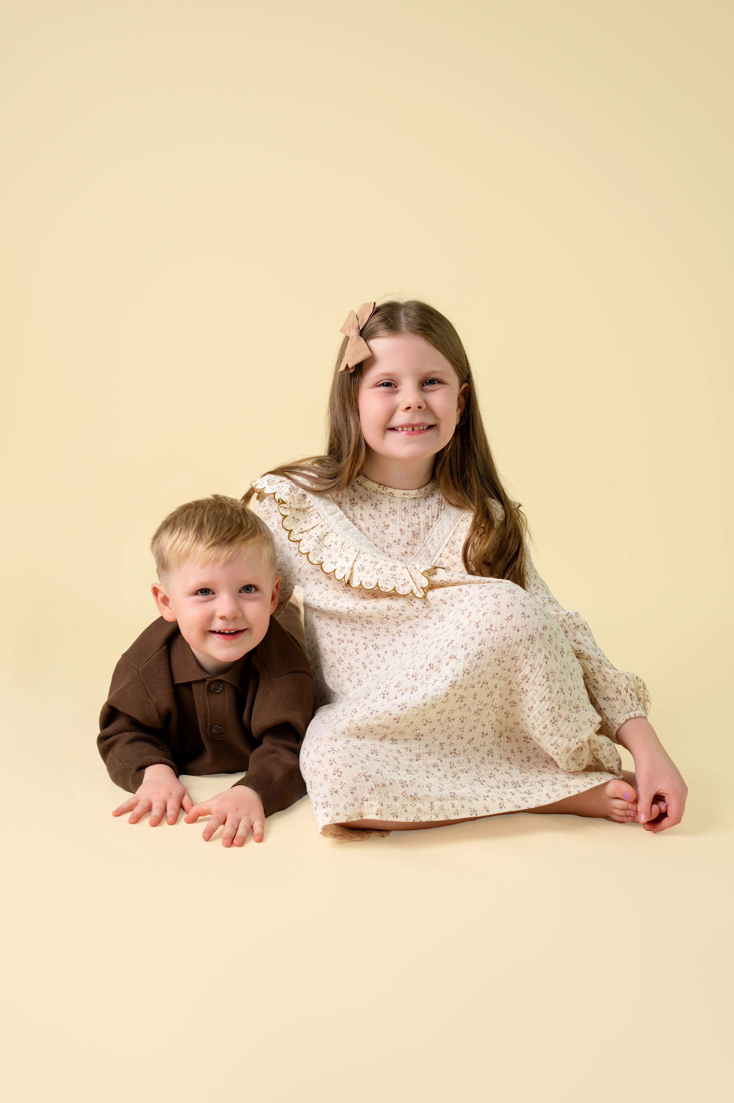 Three sequential photos of children lying on a cream colored backdrop in brown and white outfits.
