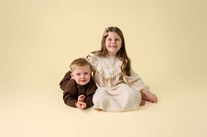 Two children lay on a beige background in a playful pose wearing matching outfits during a photo session.