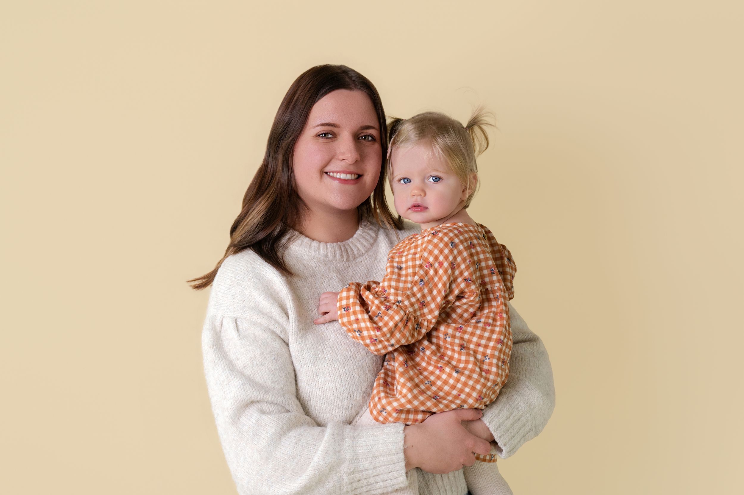 A parent in a white sweater holds a baby wearing an orange gingham outfit in a series of candid photos.