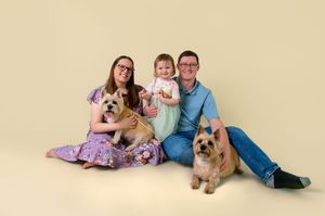 Family portrait with two German Shepherd dogs sitting on beige backdrop in studio setting.