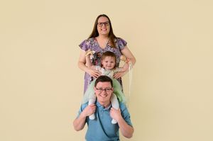 A family poses together against a beige backdrop in coordinating blue and purple outfits.