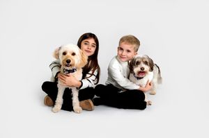 Two children sitting on white background with their fluffy pet dogs in a studio portrait setting.