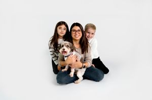 A family poses with their fluffy Australian Shepherd dog on a white background.