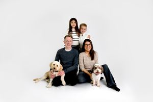 A couple sits on a white backdrop with their golden retriever dog in a series of lifestyle photos.